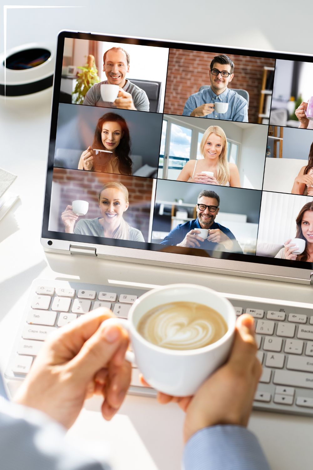 A person holds a coffee cup while participating in a virtual meeting on a laptop. The screen displays nine participants, each holding their own coffee cup and smiling, suggesting a friendly and casual online gathering.